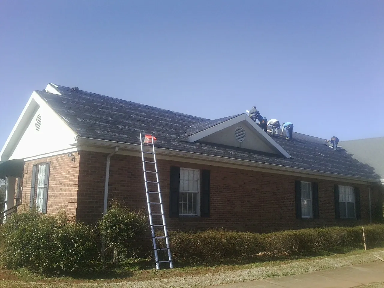 Crew tearing shingles off a brick ranch roof with a ladder set — Metal Roof Repair work by our crew in Woolwich