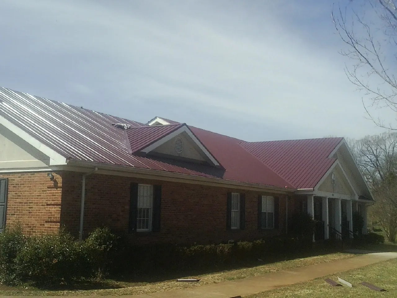 Red metal roof with gabled entries on a long brick building, from a Hail Damage Roof Repair job in Woolwich
