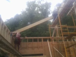 Carpenter raising a rafter beam on a new second story frame in Woolwich