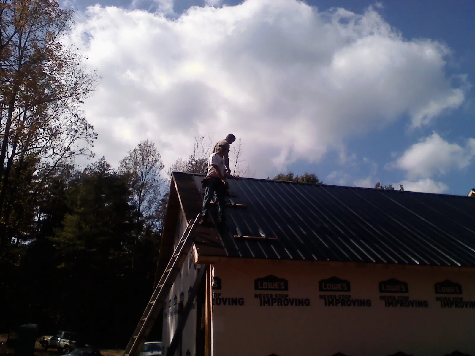 Roofer fastening dark metal panels high against a cloudy sky, from a Roof Inspection job in Woolwich